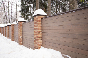 Секционный забор из планкена со столбами отделанными камнем